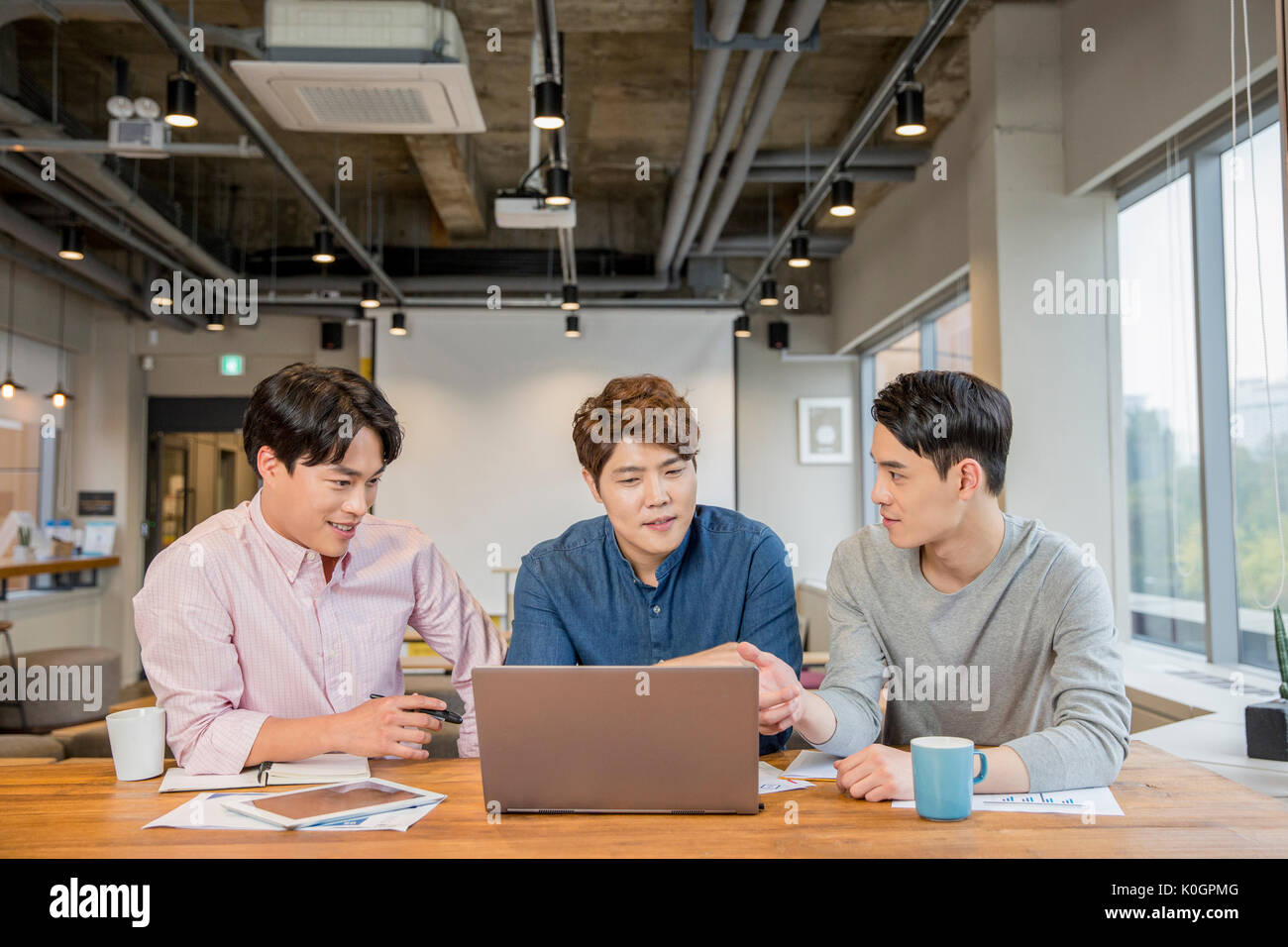 Retrato de tres empresarios sonrientes tener un encuentro compartiendo un ordenador portátil en la cafetería Foto de stock