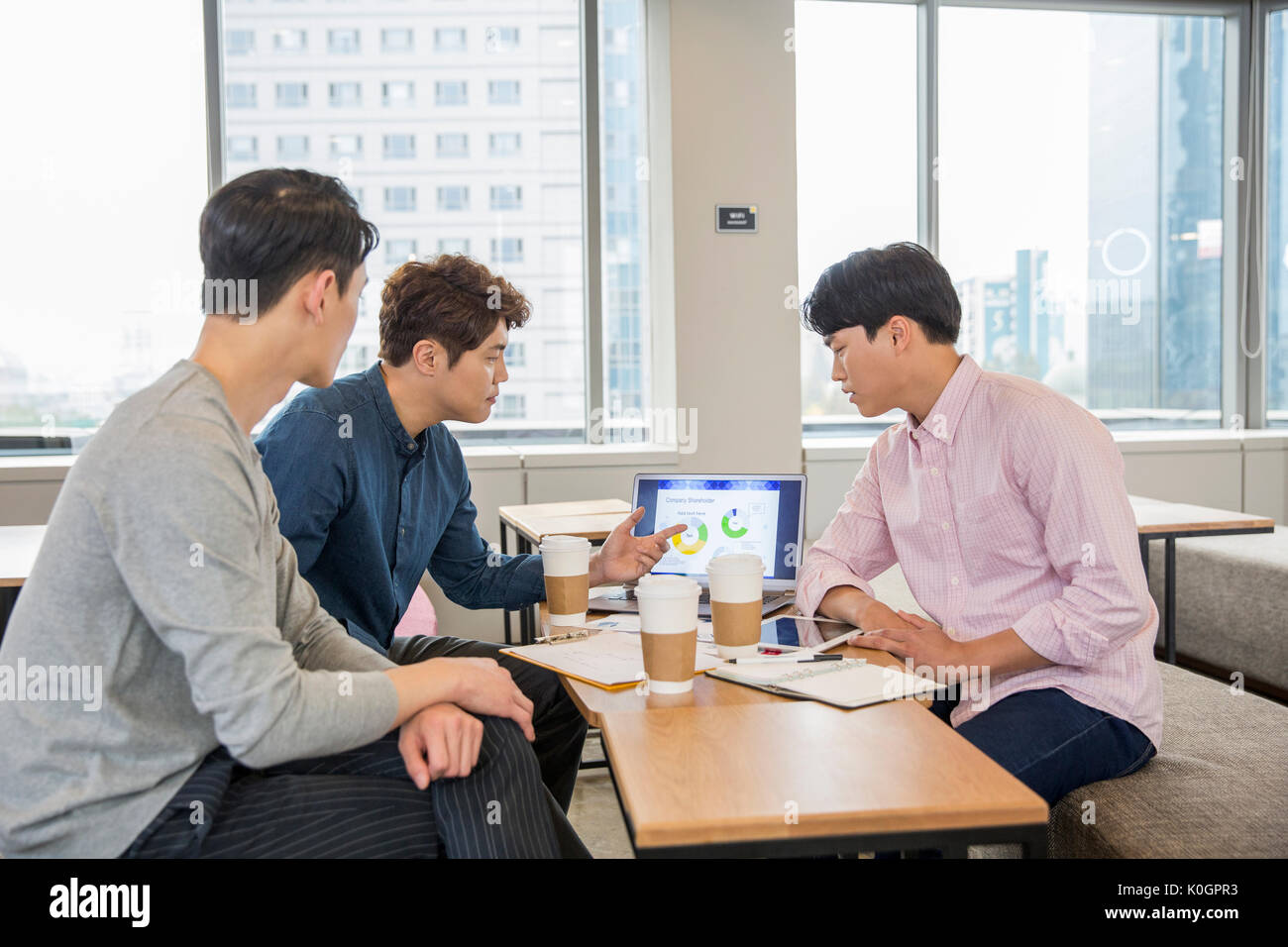 Tres empresarios tener un.encuentro compartiendo un ordenador portátil en la cafetería Foto de stock