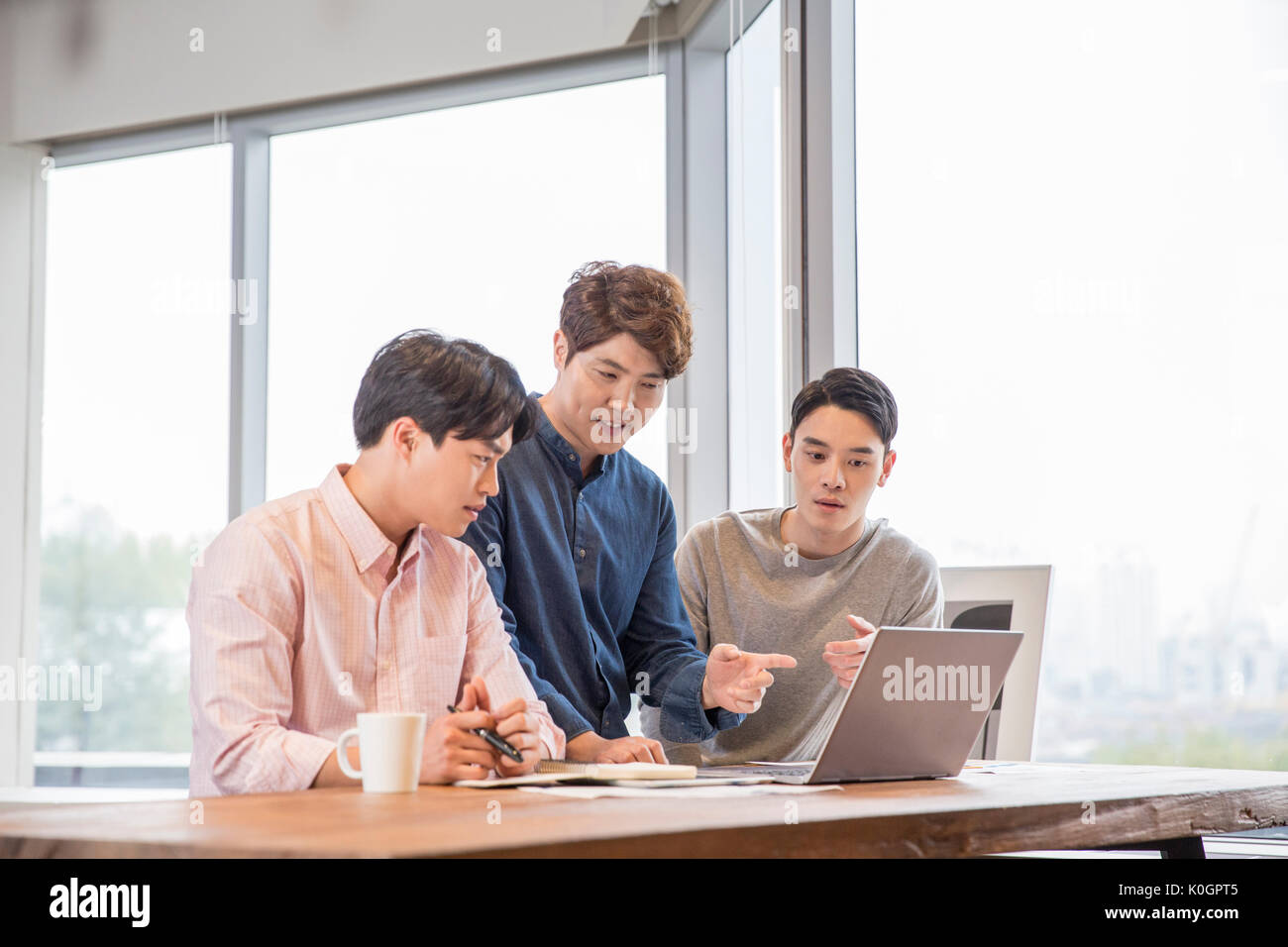 Tres empresarios sonrientes tener un encuentro compartiendo un ordenador portátil en la cafetería Foto de stock