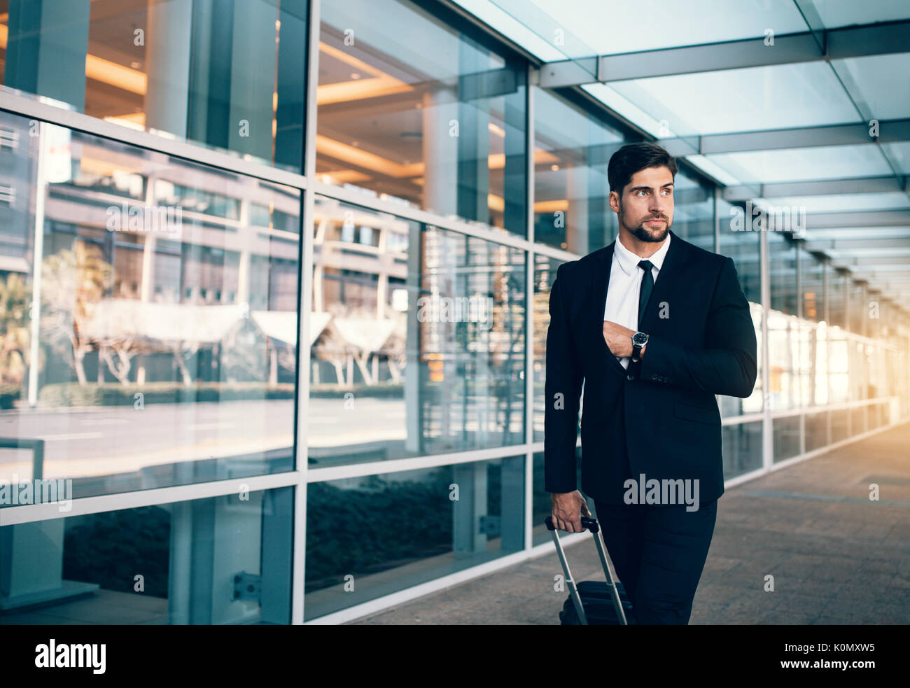 Empresario joven en viaje de negocios caminar con equipaje y mirando a otro lado. Ejecutivos de negocios, llevando la maleta en el aeropuerto. Foto de stock