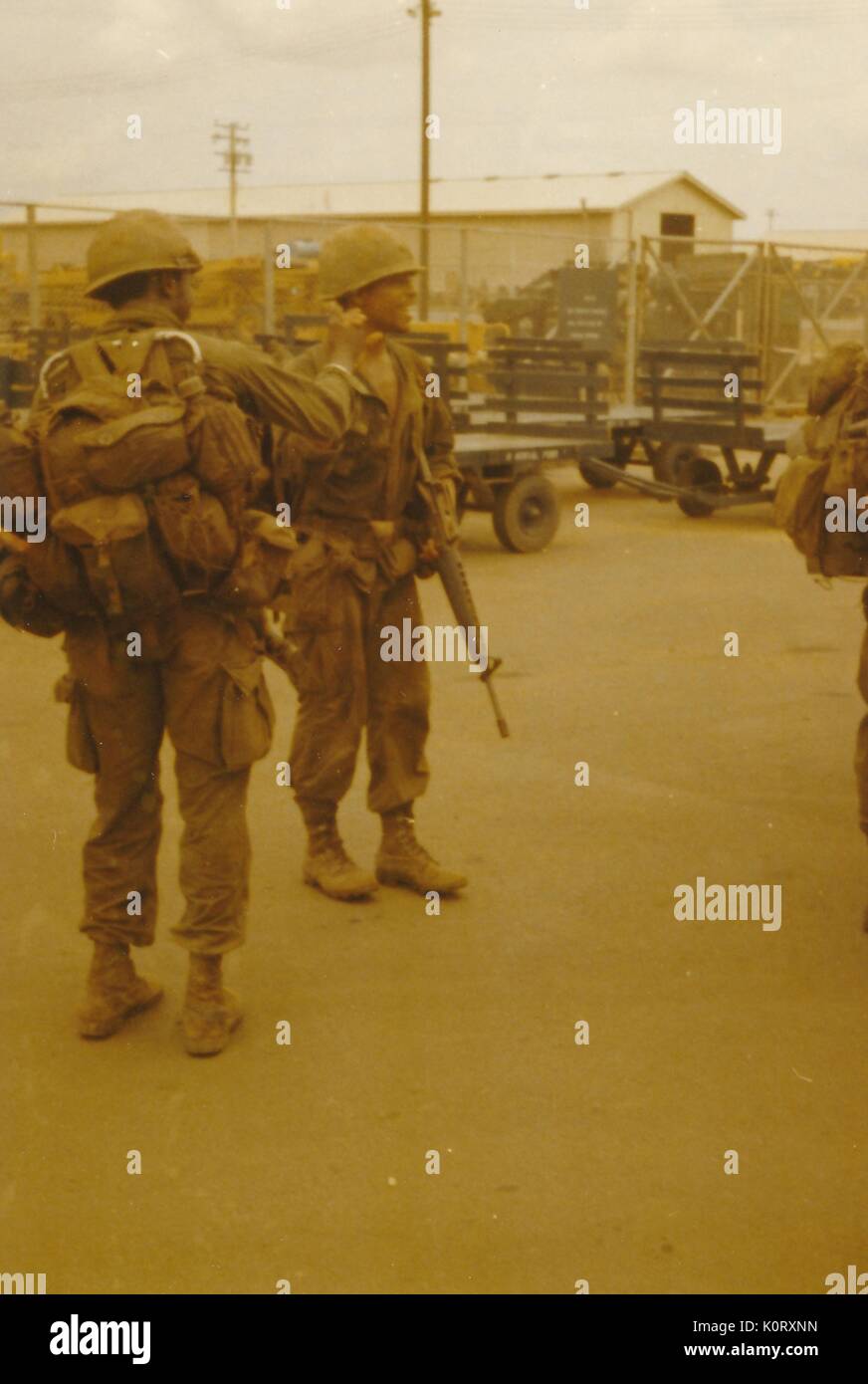 Dos soldados en plena lucha contra el engranaje compartir un momento alegre, sonriente y agarra cada otras manos, una porción de la base aérea y equipo militar conforman el fondo, la Base Aérea de Bien Hoa, Vietnam, 1964. Foto de stock