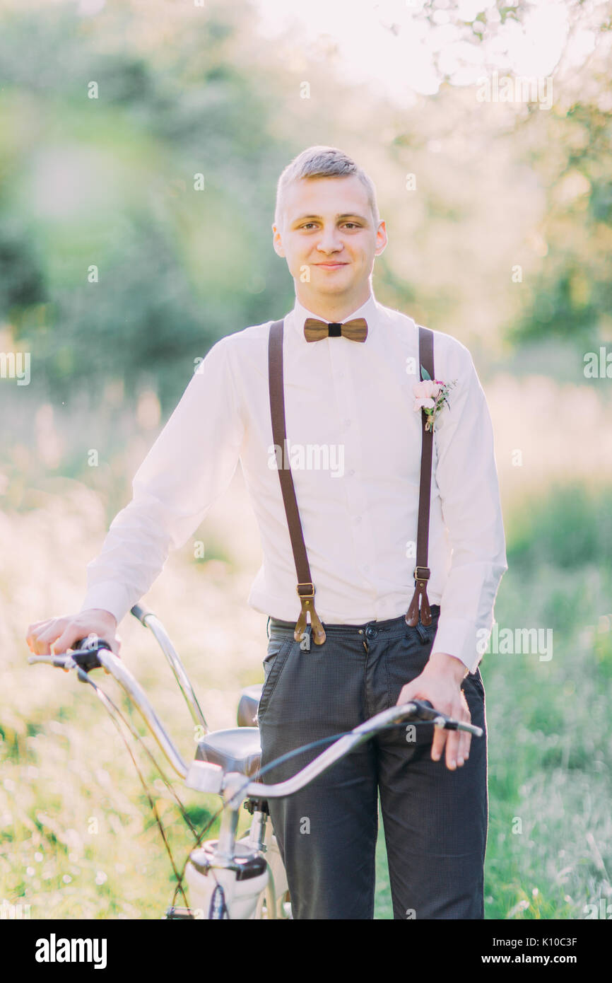 Mejor hombre sonriente en el traje oscuro y negro tirantes decorado con  flores es la celebración de la bicicleta en medio del verde campo soleado  Fotografía de stock - Alamy