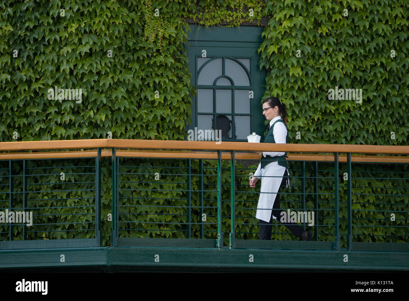 Un camarero camina pasado una ventana a los miembros alojamiento en el centro de la cancha en el Campeonato de Wimbledon 2017 Foto de stock