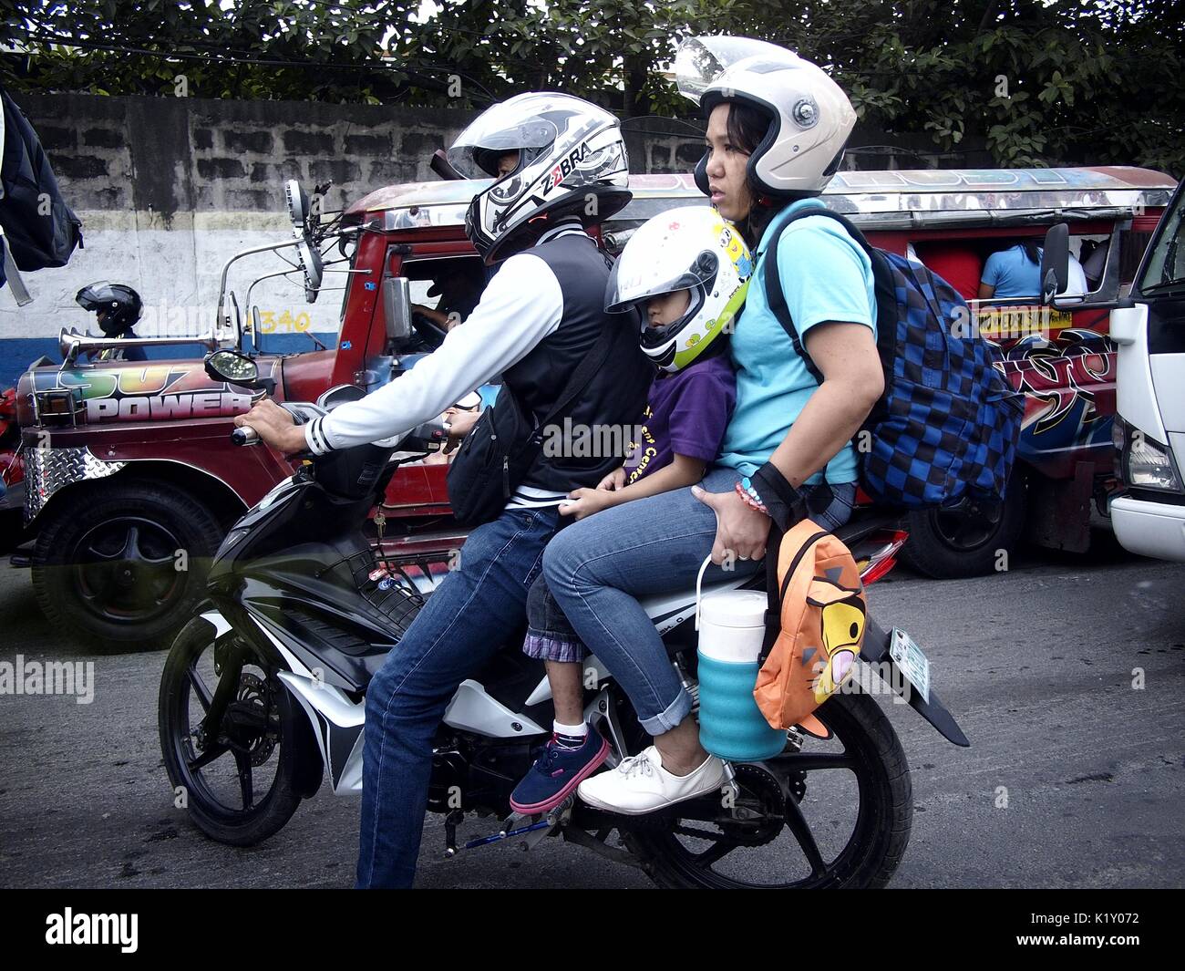 ANTIPOLO, FILIPINAS - Agosto 25, 2017: Una familia de tres personas en una motocicleta esperar el flujo de tráfico en una carretera muy transitada. Foto de stock