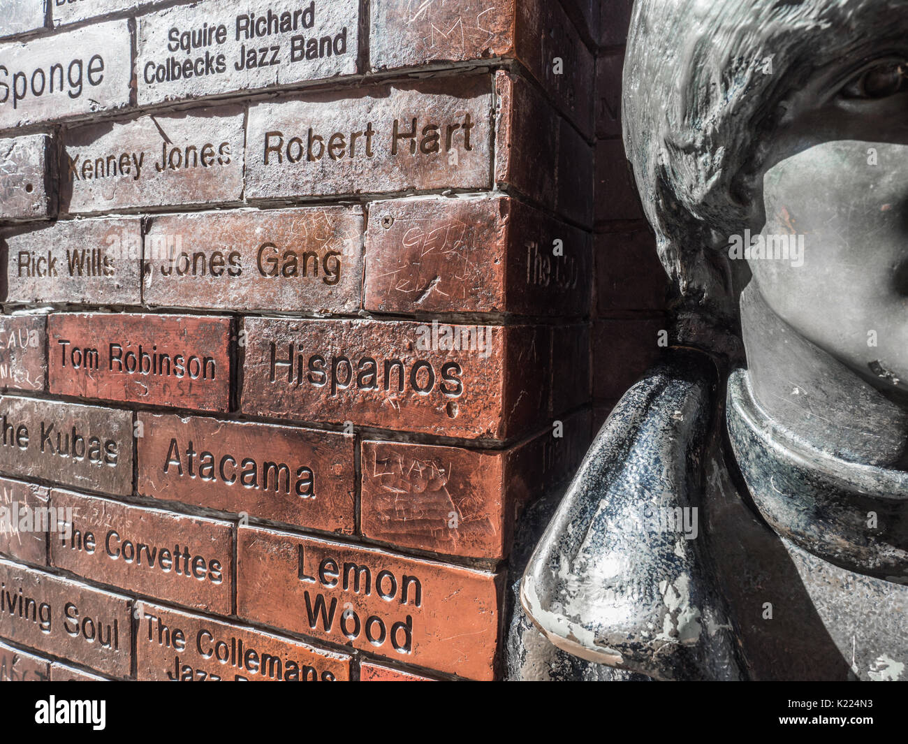 Cerca de John Lennon de los Beatles estatua con la pared de la Fama de la caverna, Mathew Street, Liverpool, Inglaterra, Reino Unido. Foto de stock