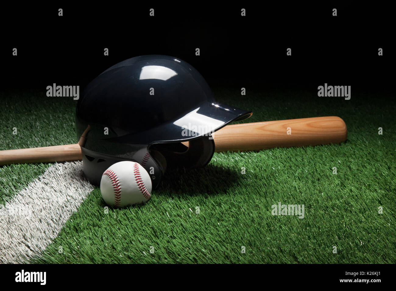 Casco de bateo de béisbol bate y pelota en campo con raya y fondo oscuro Foto de stock