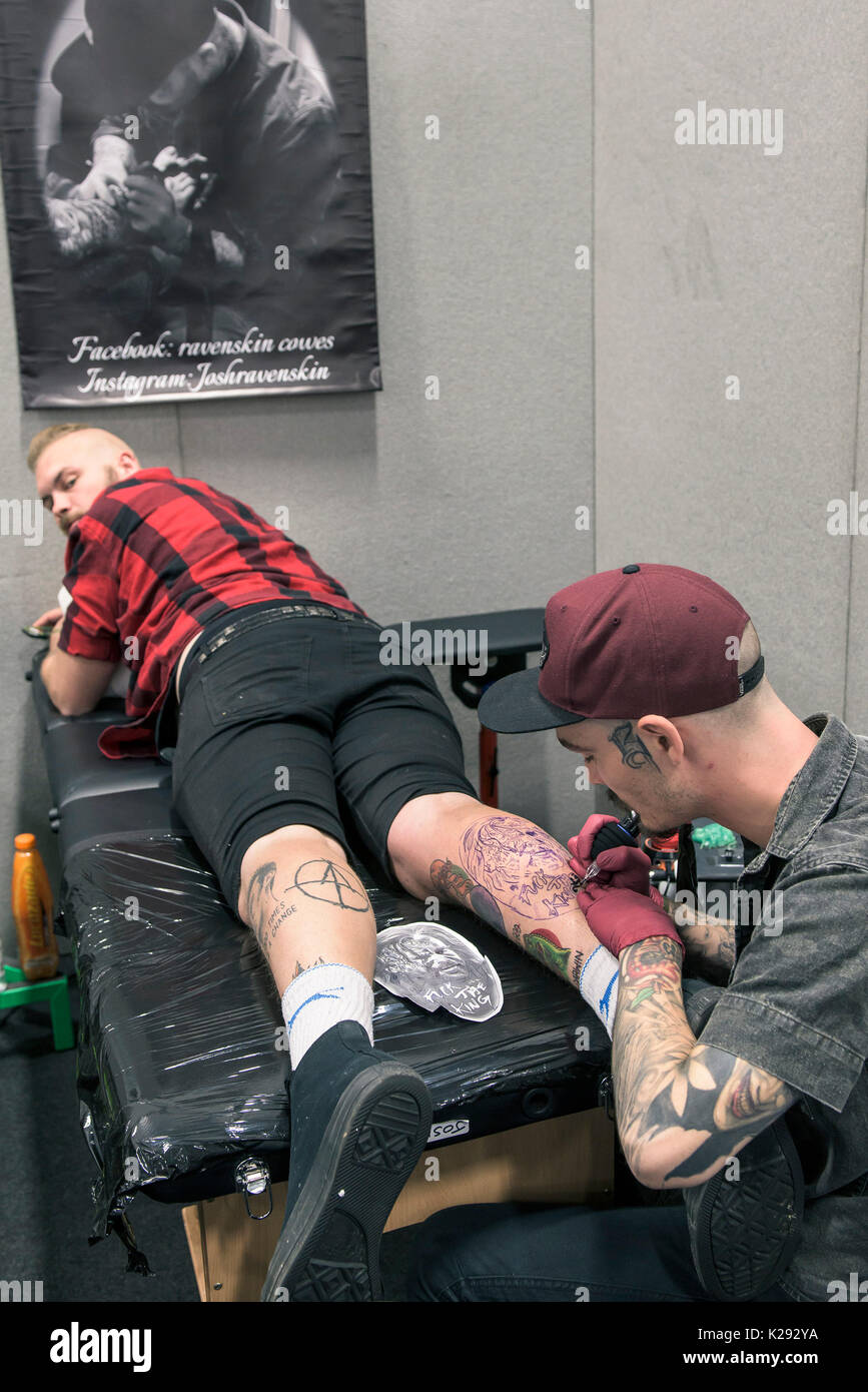 Tatuaje - Josh Docksey tatuarse la pierna de un cliente en el Cornwall Tattoo Convention. Foto de stock