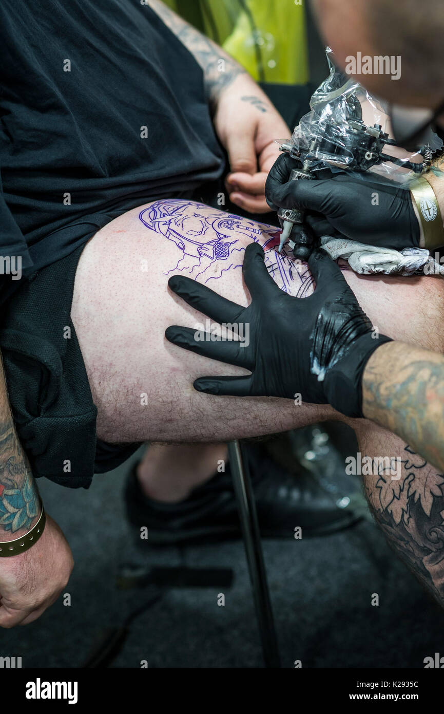 Tatuaje. Un tattooist aplicando un diseño a un cliente en el muslo Cornwall Tattoo Convention. Foto de stock