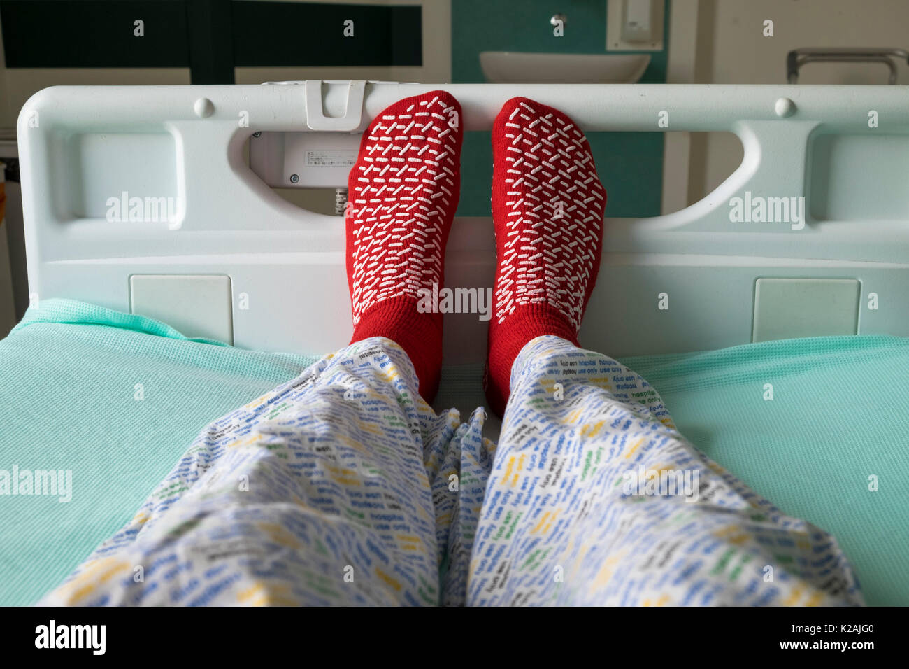 Paciente acostado en una cama de hospital con uso hospitalario solo partes de abajo de pijama y calcetines antideslizantes, sala de aislamiento, reino unido Foto de stock