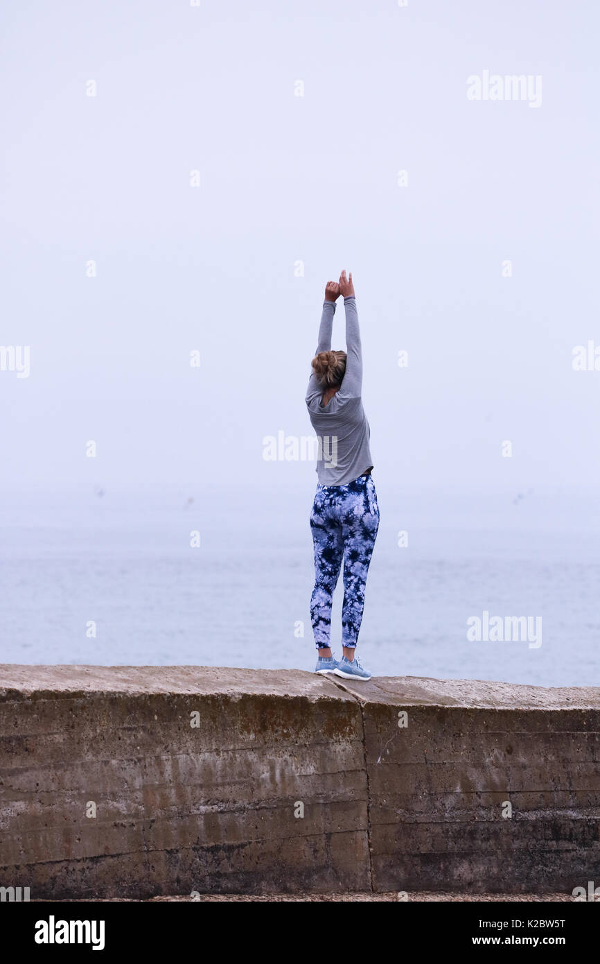 Mujer joven haciendo yoga en la escollera en Cromer, Norfolk, Reino Unido. Foto de stock