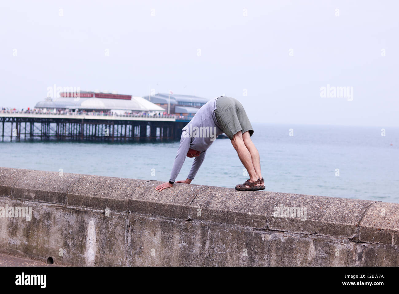 Hombre de 50 años, haciendo una pose de yoga perro boca abajo sobre la escollera en Cromer, Norfolk, Reino Unido. Foto de stock