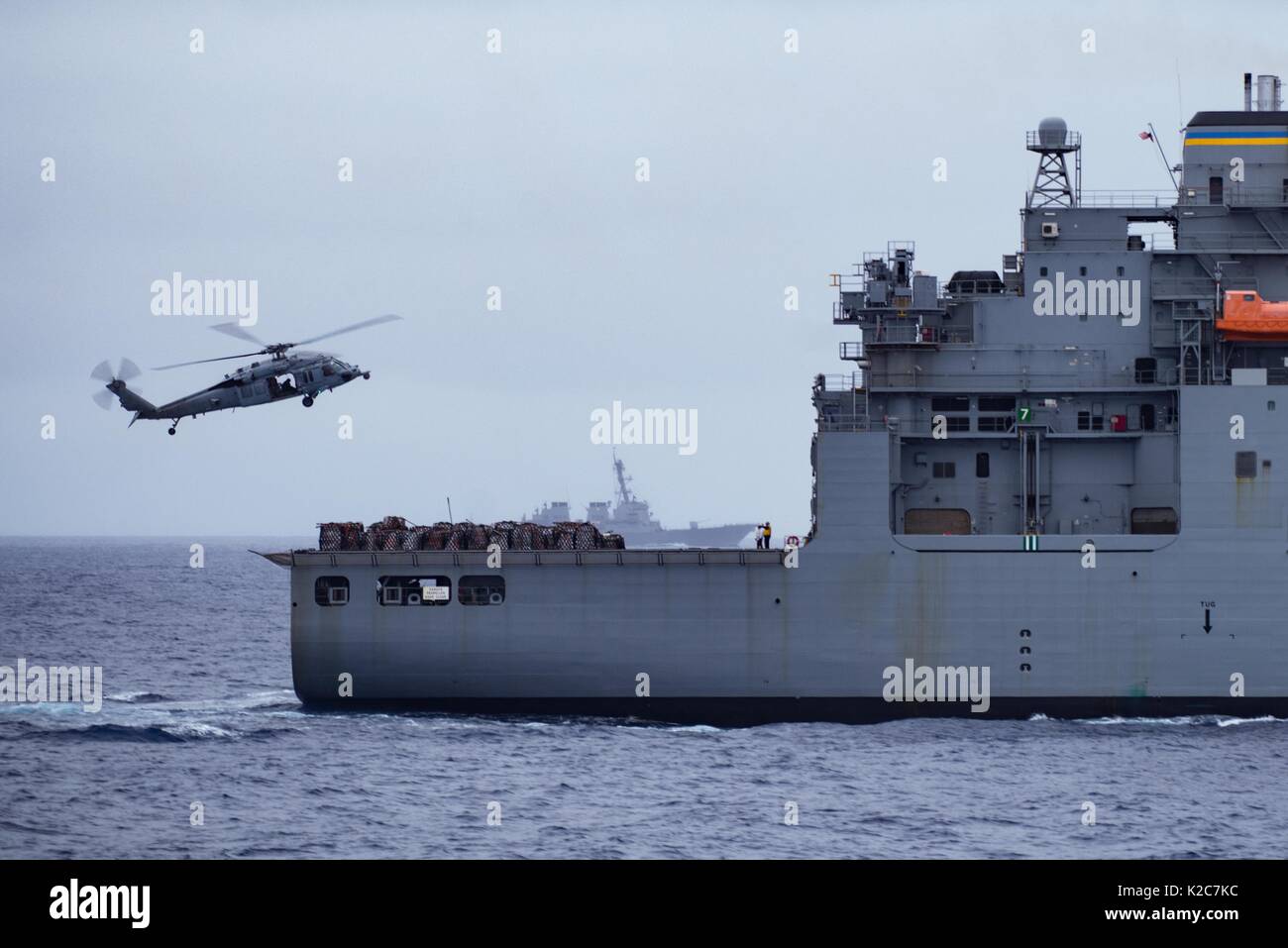 Marina MH-60 Seahawk helicóptero recoge los suministros procedentes de la Marina de los EE.UU. Lewis y Clark clase municiones de carga seca buque USNS Matthew Perry el 15 de agosto de 2017 en el Océano Pacífico. Foto de stock