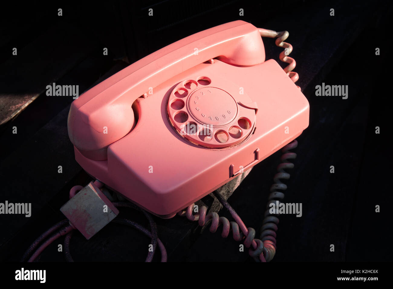 Iluminado de color rosa vintage retro teléfono usado contra el fondo oscuro. La tecnología de la comunicación del pasado. Foto de stock