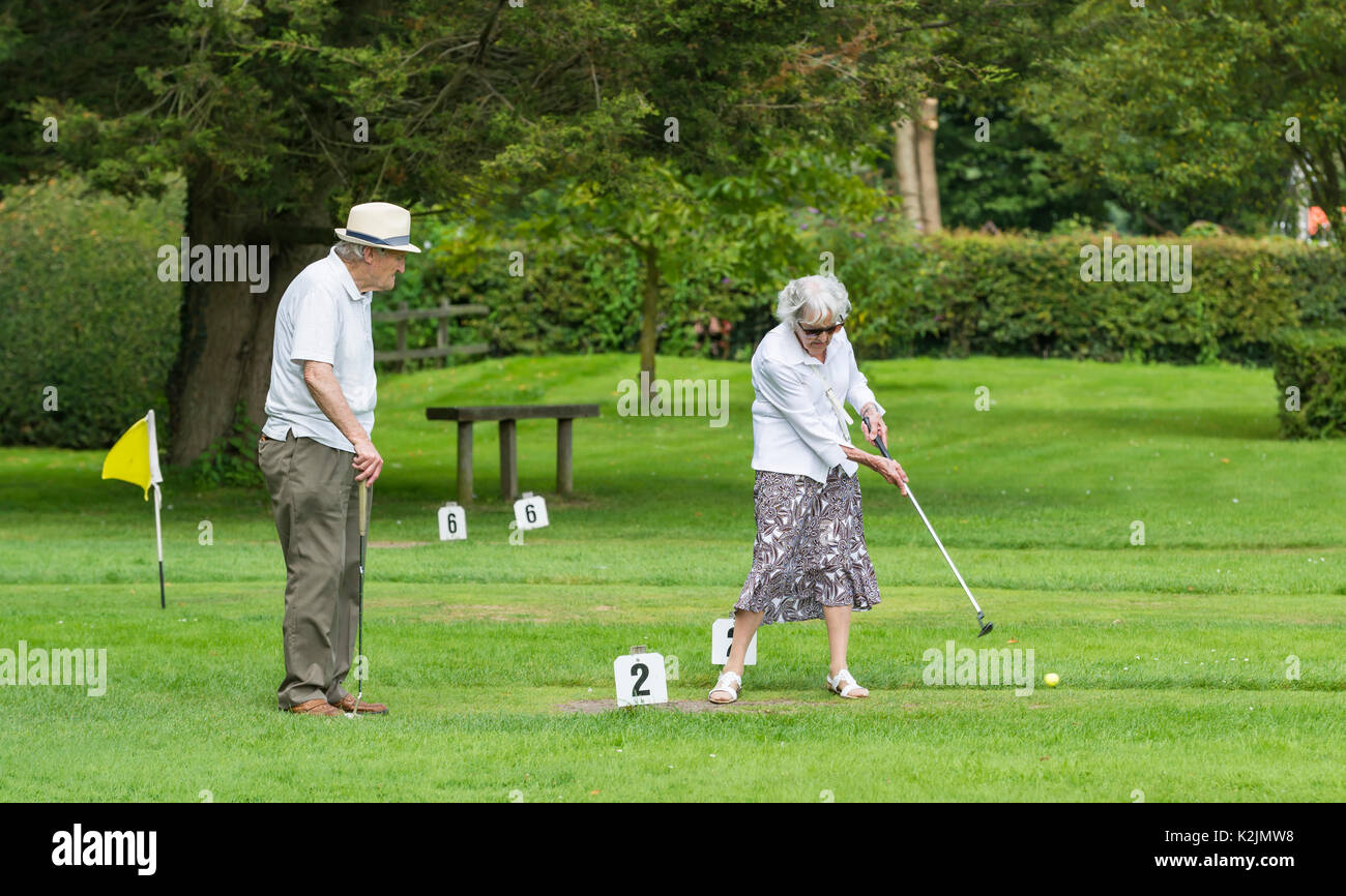Pareja de ancianos jugando poniendo en un pequeño campo de golf en verano en el Reino Unido. Active los pensionistas. Foto de stock