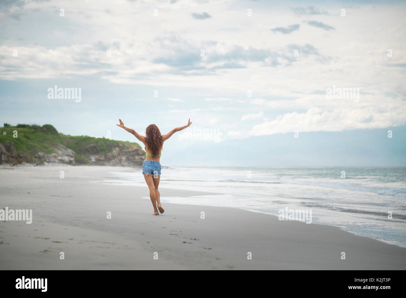 Mujer atractiva elevando los brazos caminando felices en una playa Foto de stock