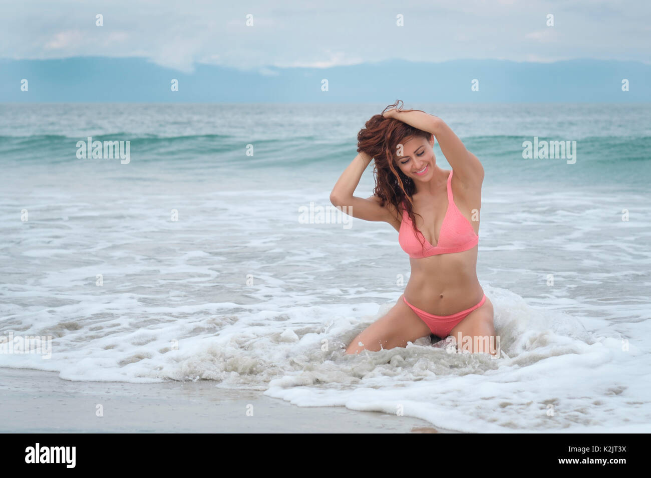 La mujer hispana en bikini sonriendo felizmente mientras está sentado en el agua Foto de stock