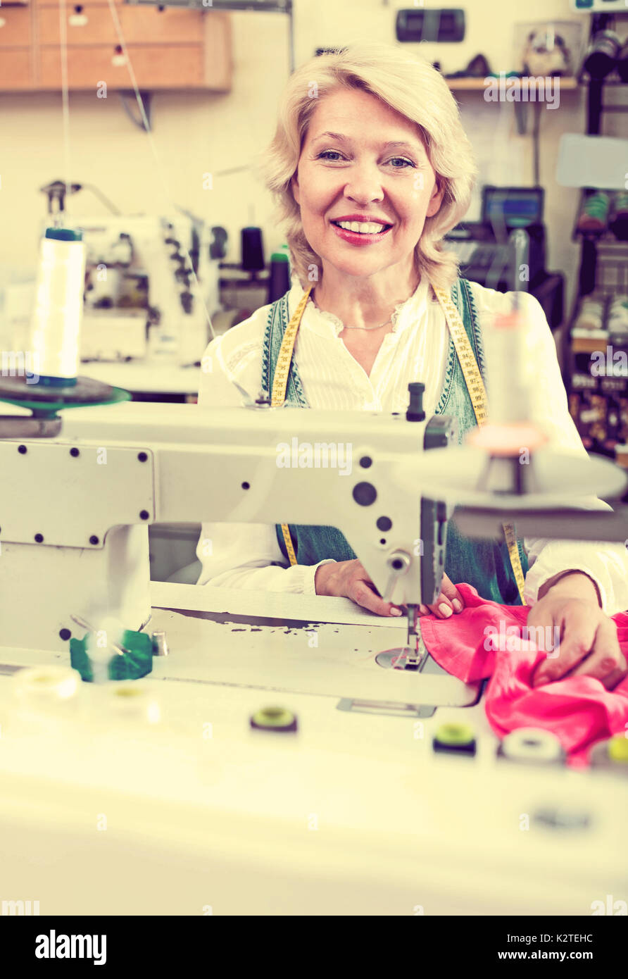 Alegre mujer senior coser con máquina profesional en un taller Foto de stock