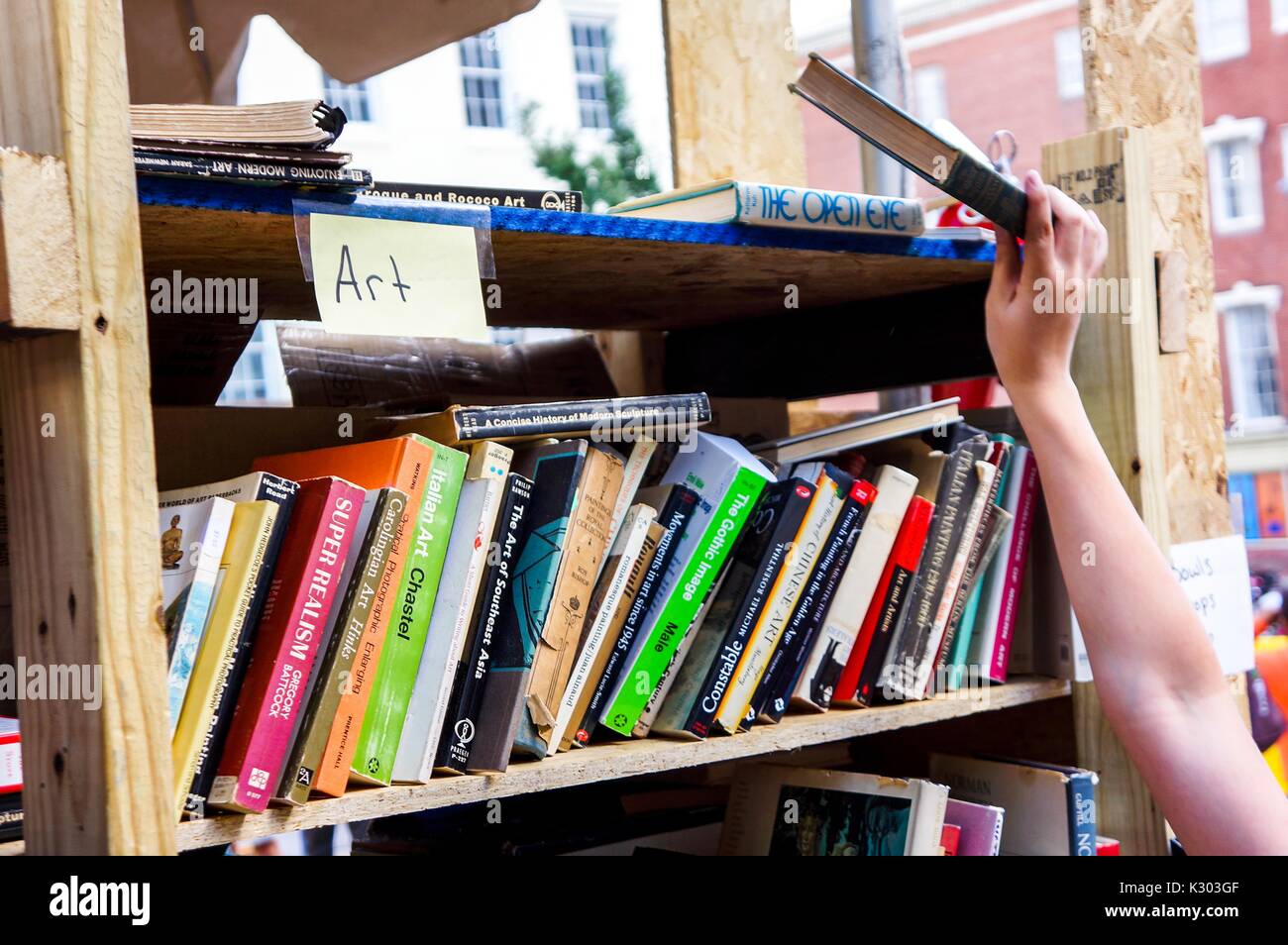 Una mano alcanza para un libro en el estante superior de un carro etiquetados como 'arte, ' con libros usados para la venta durante el Festival del Libro de Baltimore, Baltimore, Maryland, septiembre de 2013. Foto de stock