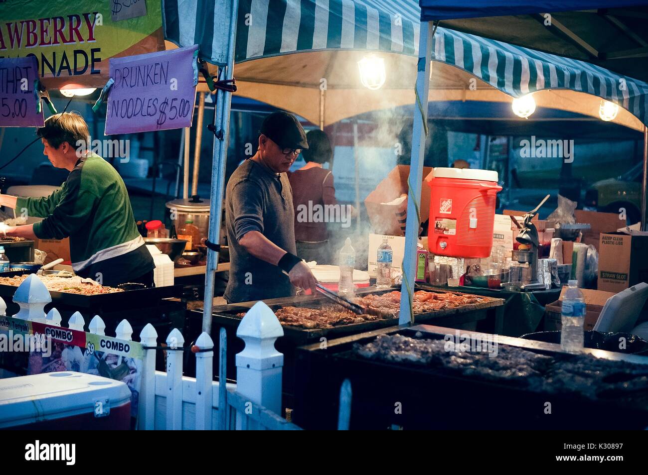 Dos hombres de pie delante de grandes Parrilladas cocinar el pollo en brochetas en un stand de alimentos al anochecer, durante la Feria de Primavera, un estudiante-run carnaval de primavera en la Universidad Johns Hopkins, Baltimore, Maryland, abril de 2016. Cortesía de Eric Chen. Foto de stock