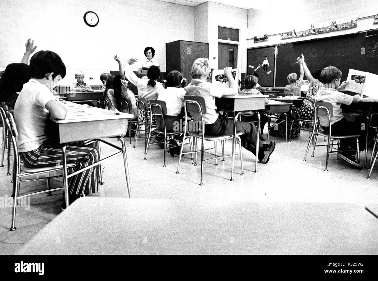 En una demostración de la escuela elemental de la Universidad Johns Hopkins, niños y niñas se sientan en pupitres en un aula, mientras que la maestra está al lado de la habitación, y varios estudiantes levantar sus manos para responder una pregunta, Baltimore, Maryland, junio de 1975. Foto de stock