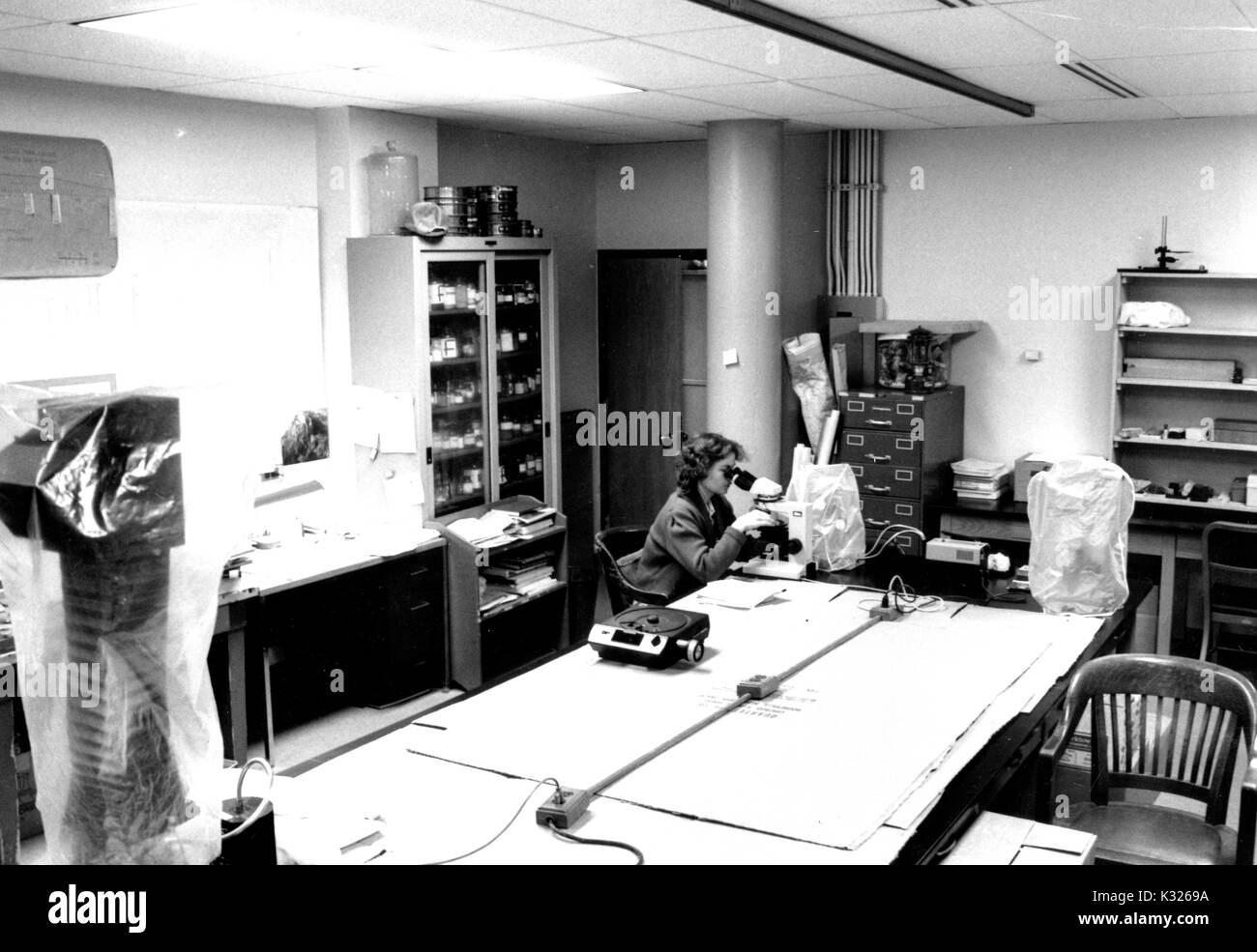 En el interior de la sedimentología Laboratorio de Lawrence A. Hardie en Olin Hall -- la Tierra y el edificio de Ciencias Planetarias en la Universidad Johns Hopkins -- un científico femenino está sola en el borde de una tabla larga mirando a través de un microscopio, rodeado de equipos y materiales de laboratorio, Baltimore, Maryland, en 1986. Foto de stock