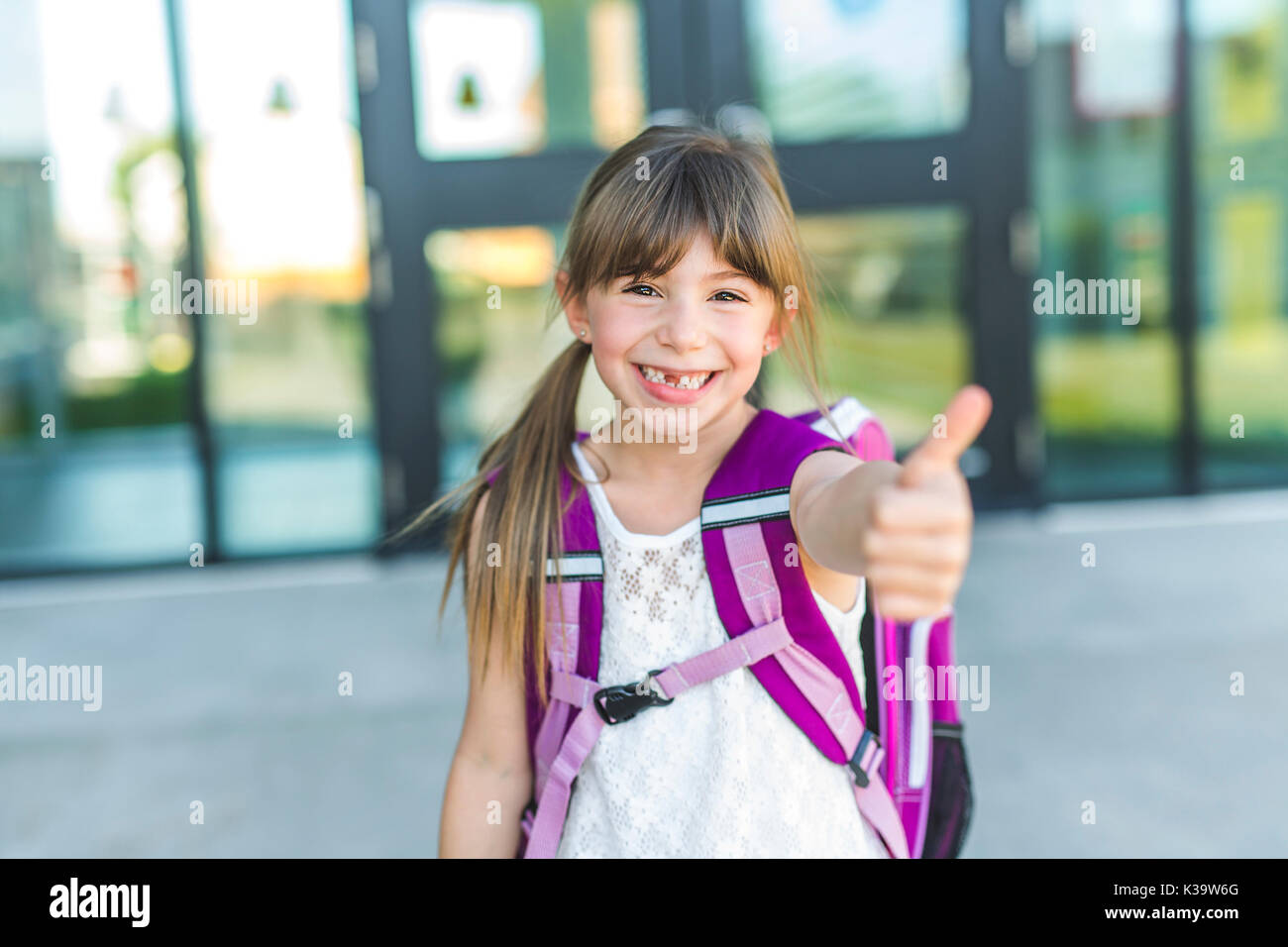 Chica de pie fuera de la escuela con bolsa Foto de stock