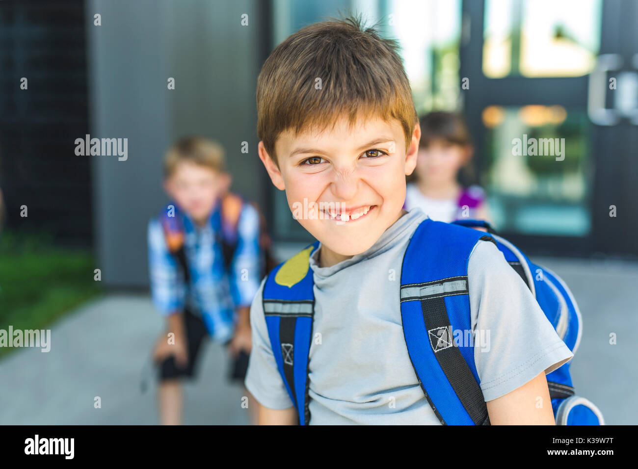 Niño de pie fuera de la escuela con bolsa Foto de stock