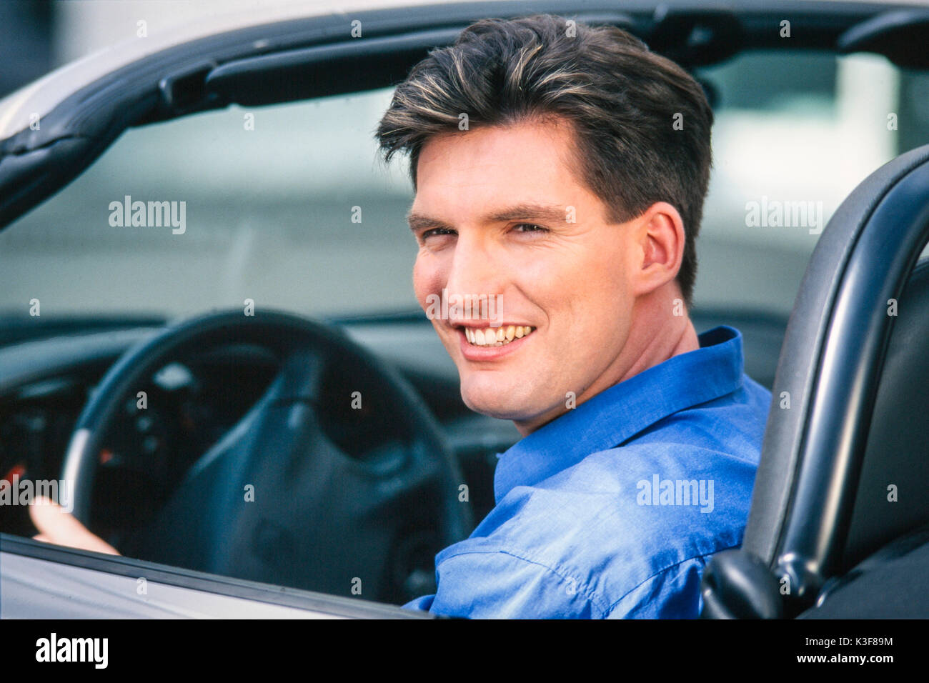 Hombre joven está sentado en el coche y risas Foto de stock