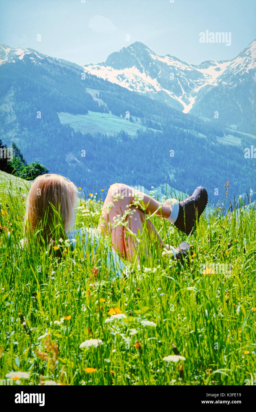 Mujer joven radica en la pradera delante del paisaje montañoso, Alpbachtal, Tirol Foto de stock
