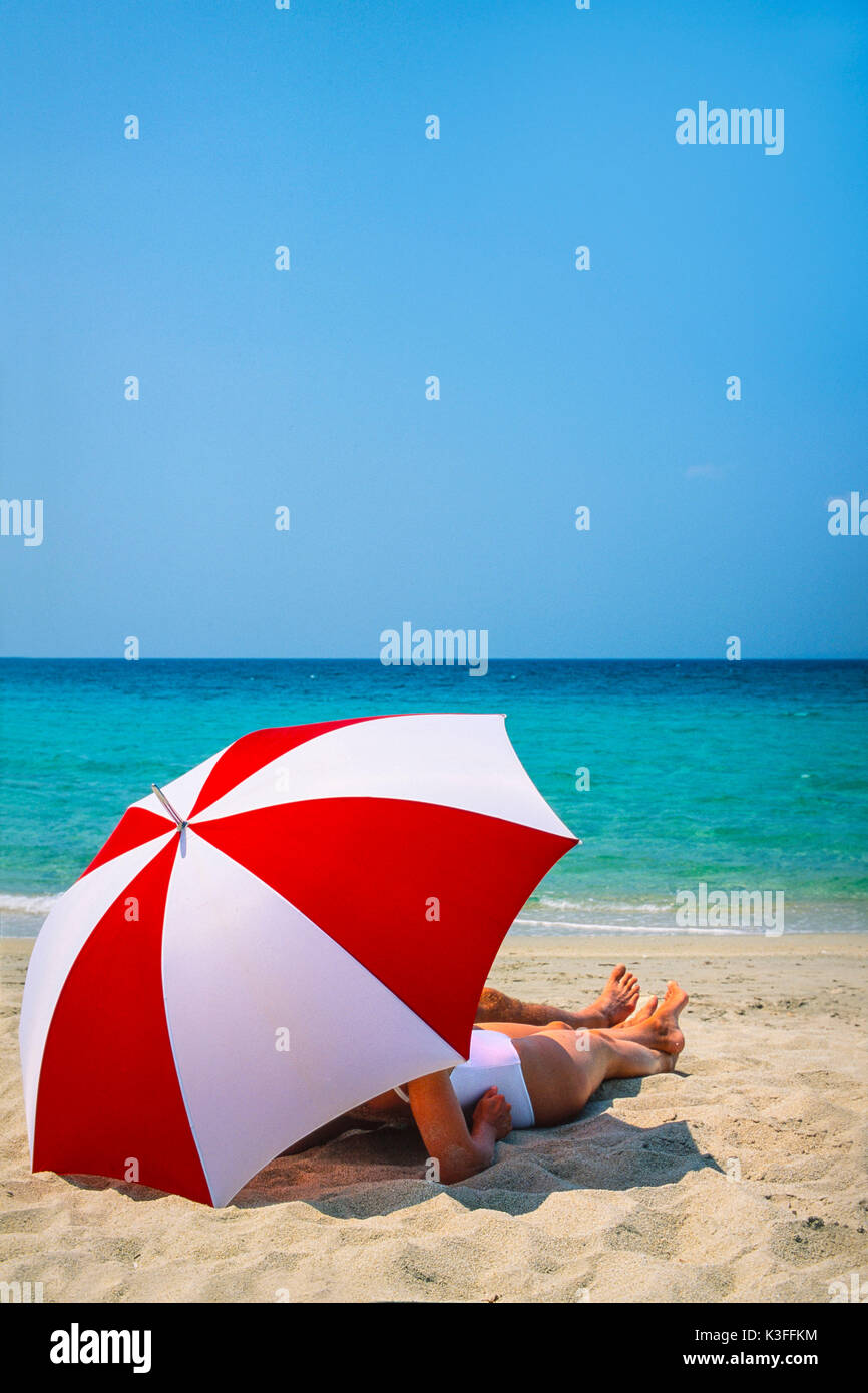 La pareja se encuentra bajo una sombrilla en la playa. Foto de stock