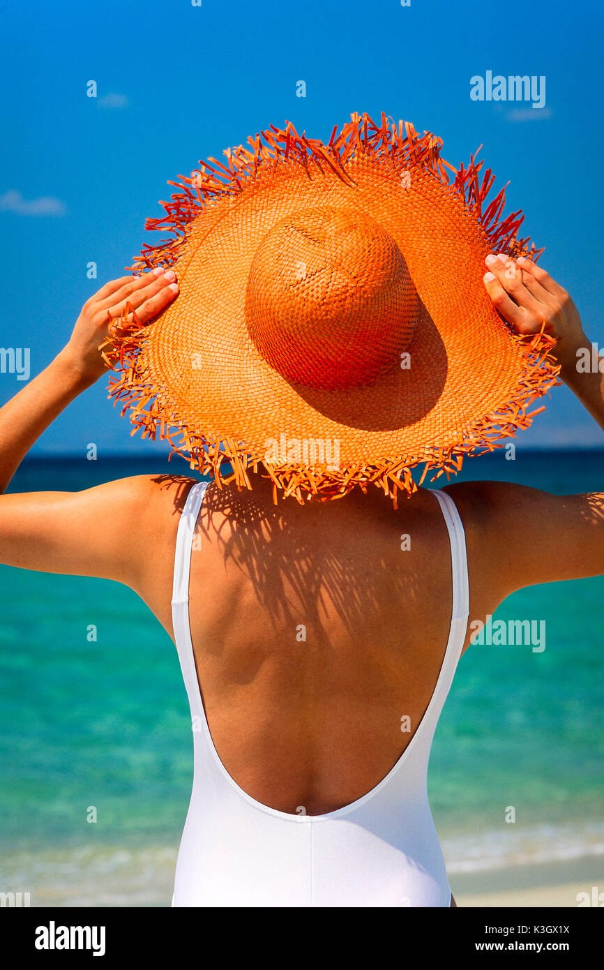 Mujer de la vuelta a la playa, posee en su sombrero para el sol Foto de stock