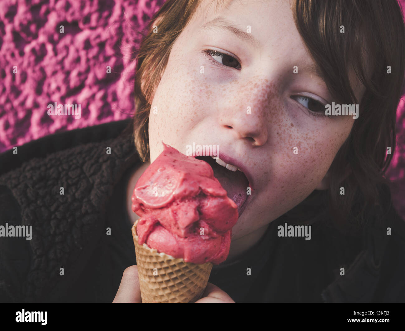 Retrato de un joven comer helado de fresa delante de un fondo de color rosa Foto de stock