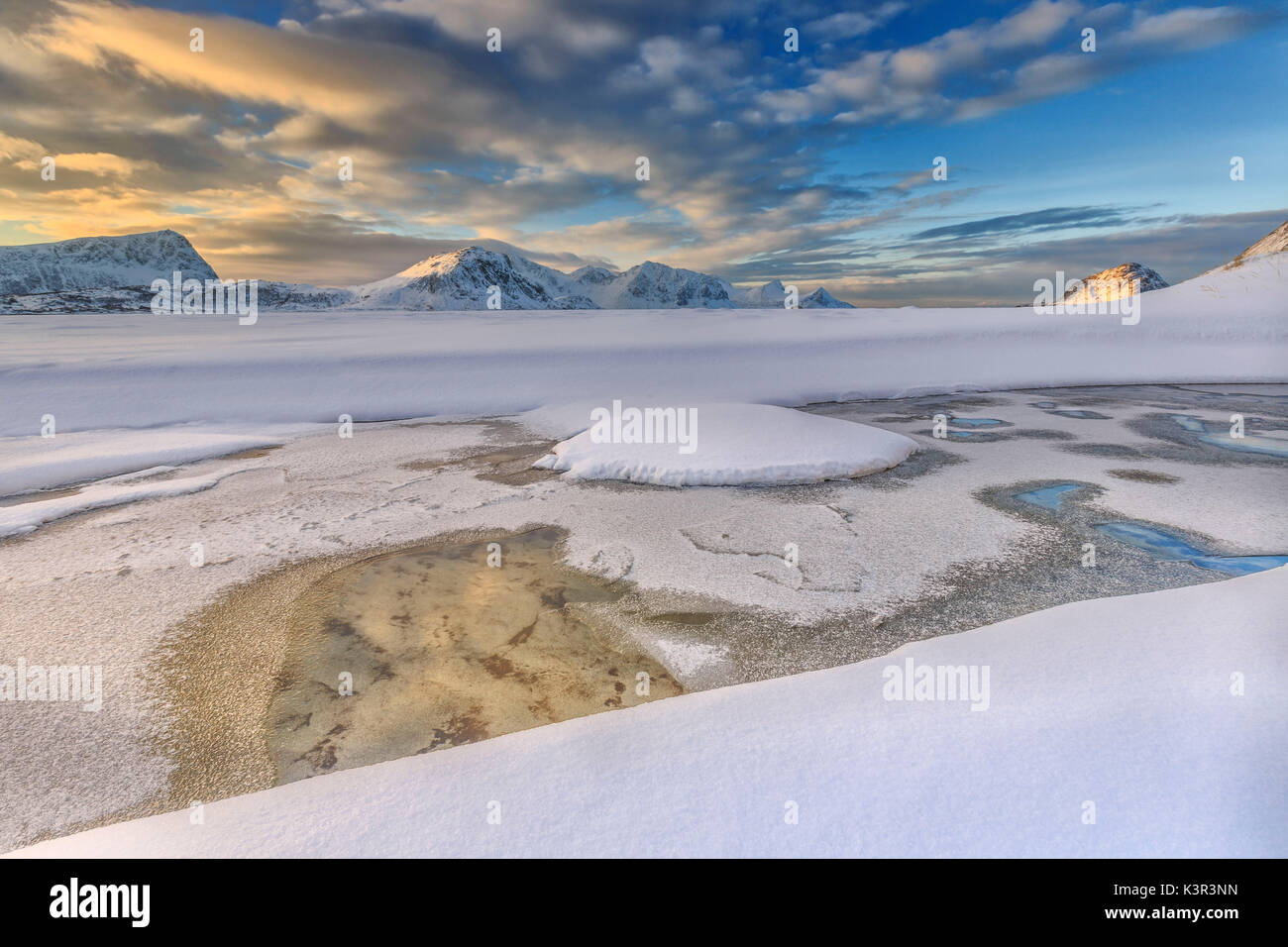 El amanecer dorado se refleja en una piscina de aguas cristalinas donde la nieve es casi derretido. Las Islas Lofoten Noruega Europa Haukland Foto de stock