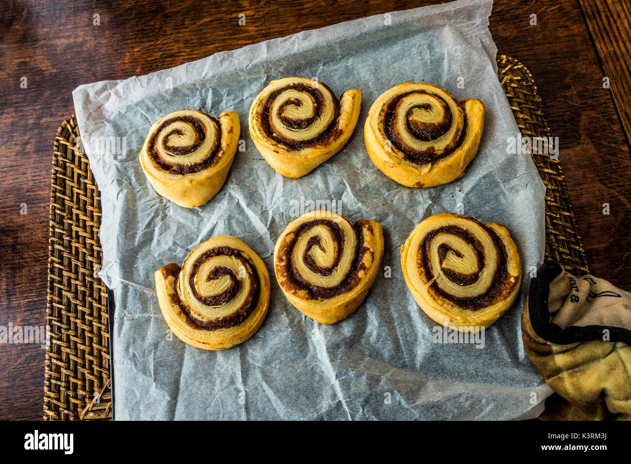 Caliente, canela pastelería casera, remolinos, directamente desde el horno, en una bandeja de papel resistente a la grasa, que se celebró por un guante acolchado. Inglaterra, Reino Unido. Foto de stock