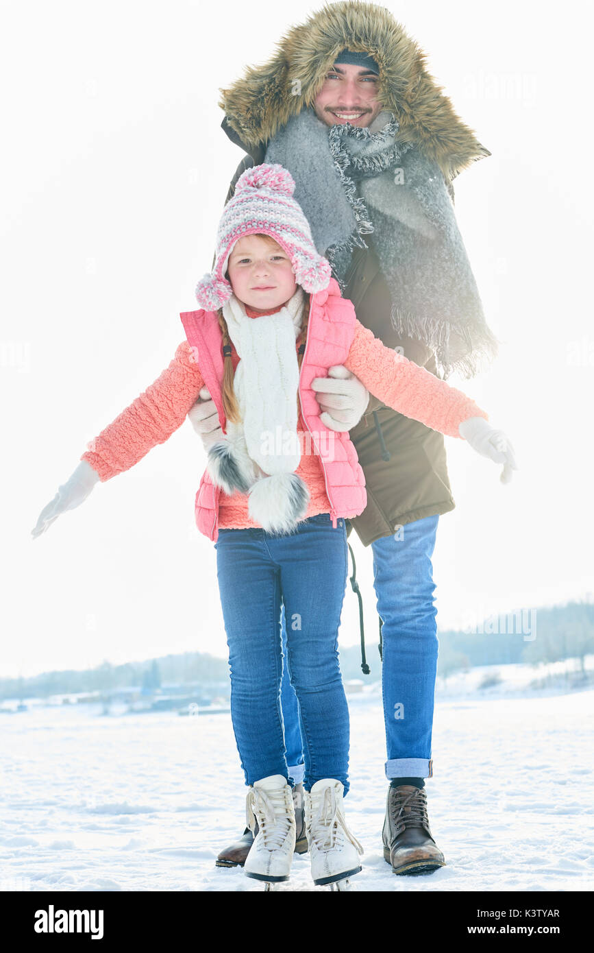 Hija de padre ayuda con el aprendizaje de patinaje sobre hielo en invierno Foto de stock