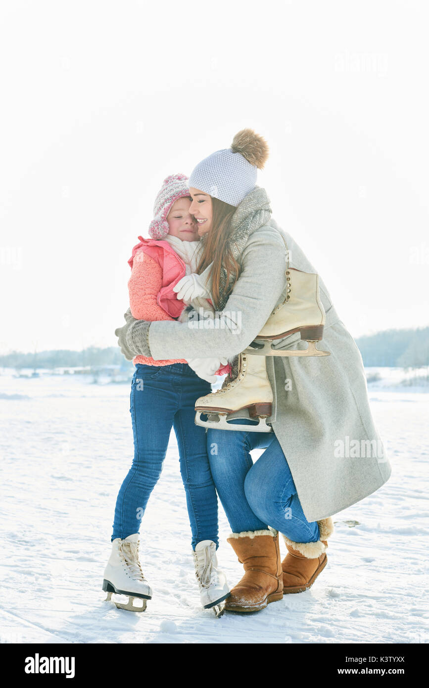 Feliz madre abraza a su hija en invierno, mientras que el patinaje sobre hielo Foto de stock
