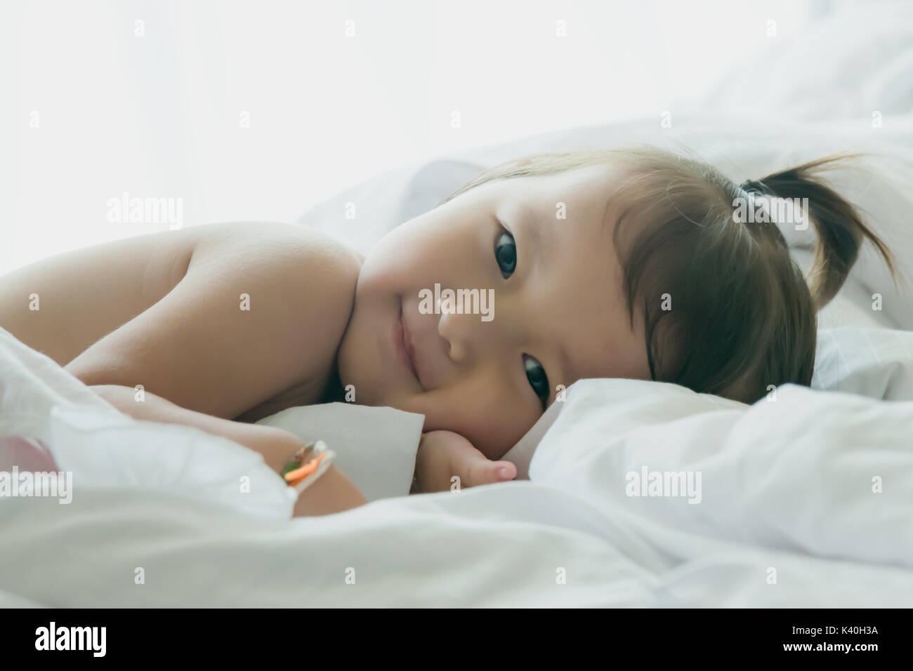 Niño acostado sonrisa en ropa de cama blanca habitación con espacio de copia.:centrado suave Foto de stock