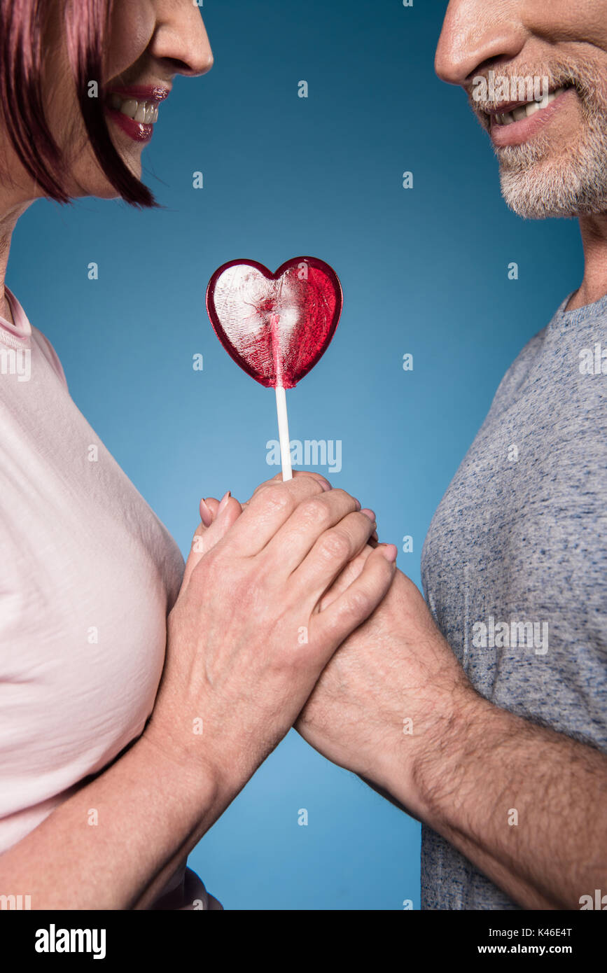 Captura recortada de la pareja de ancianos tomados de la mano con la piruleta en forma de corazón Foto de stock