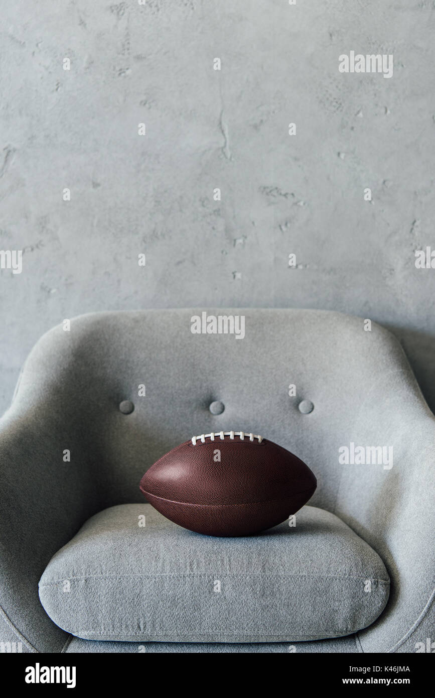 Balón de fútbol americano en textil gris sillón en la habitación vacía Foto de stock