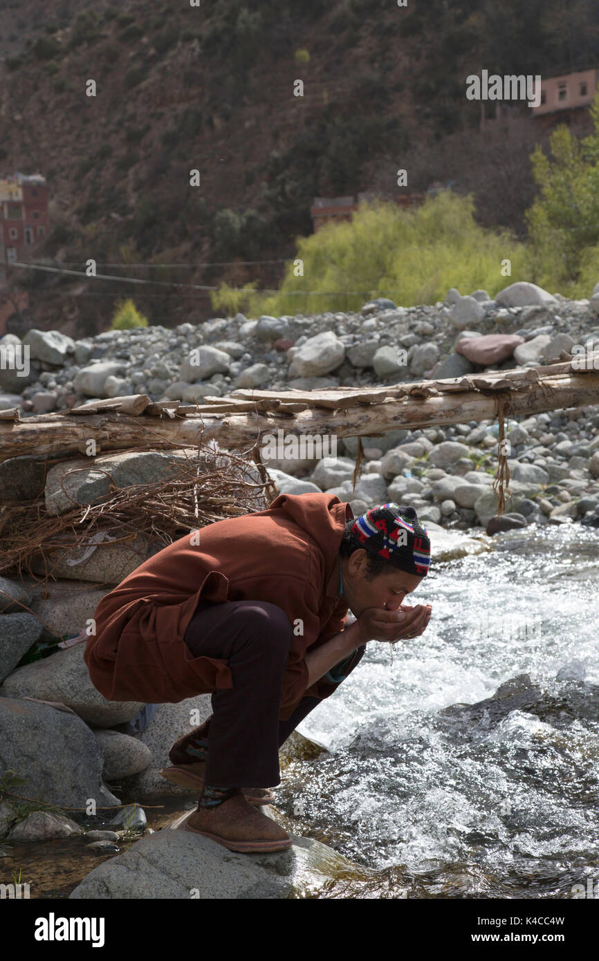 El bereber Hombre bebiendo de río, Setti Fatma mercado, valle de Ourika, Marruecos Foto de stock