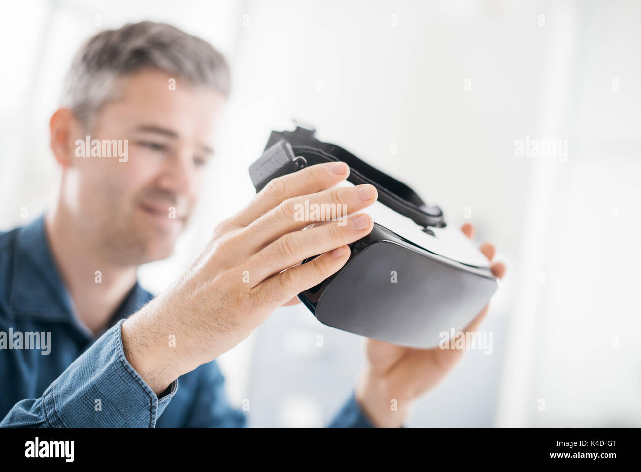 Hombre sujetando un casco de realidad virtual y sonriente, innovador concepto de tecnología Foto de stock