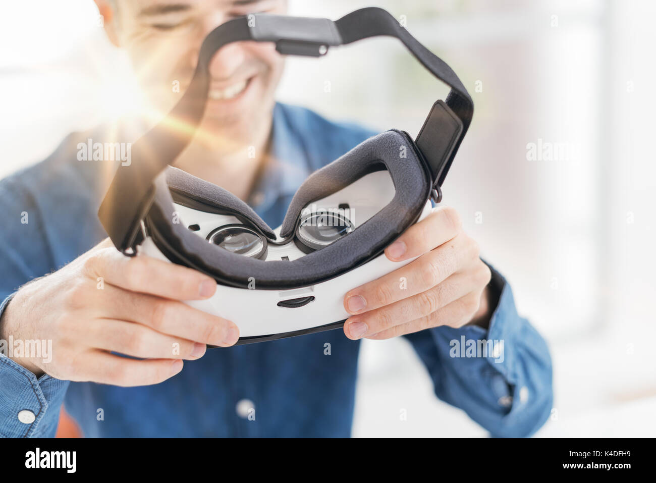 Hombre sujetando un casco de realidad virtual y sonriente, innovador concepto de tecnología Foto de stock