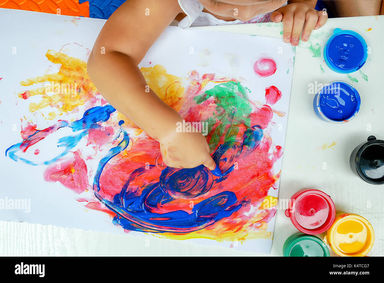La pintura de la muchacha pequeña por el color de la mano del dedo, la imaginación ilimitada ilimitada ilimitada a través de carteles de color pastel mezclados en un escritorio de la fiesta que no va al concepto del desarrollo de school.children. Foto de stock
