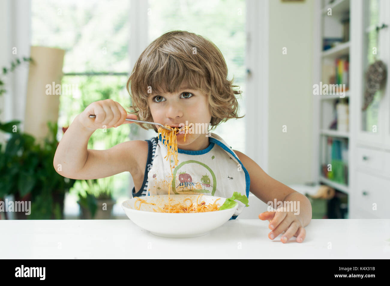 Retrato de un joven muchacho lindo haciendo un lío mientras comer pasta para el almuerzo Foto de stock