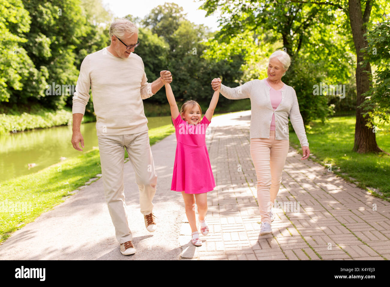 Familia, generación y la gente sonríe feliz concepto - la abuela, abuelo y nieta poco caminando en park Foto de stock