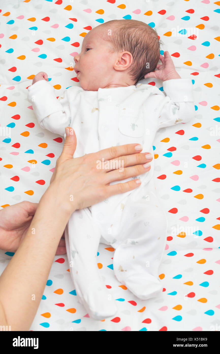 Bebé recién nacido vestidos de blanco tendido sobre su espalda, con cólicos; madre la mano sobre su barriga Fotografía de - Alamy