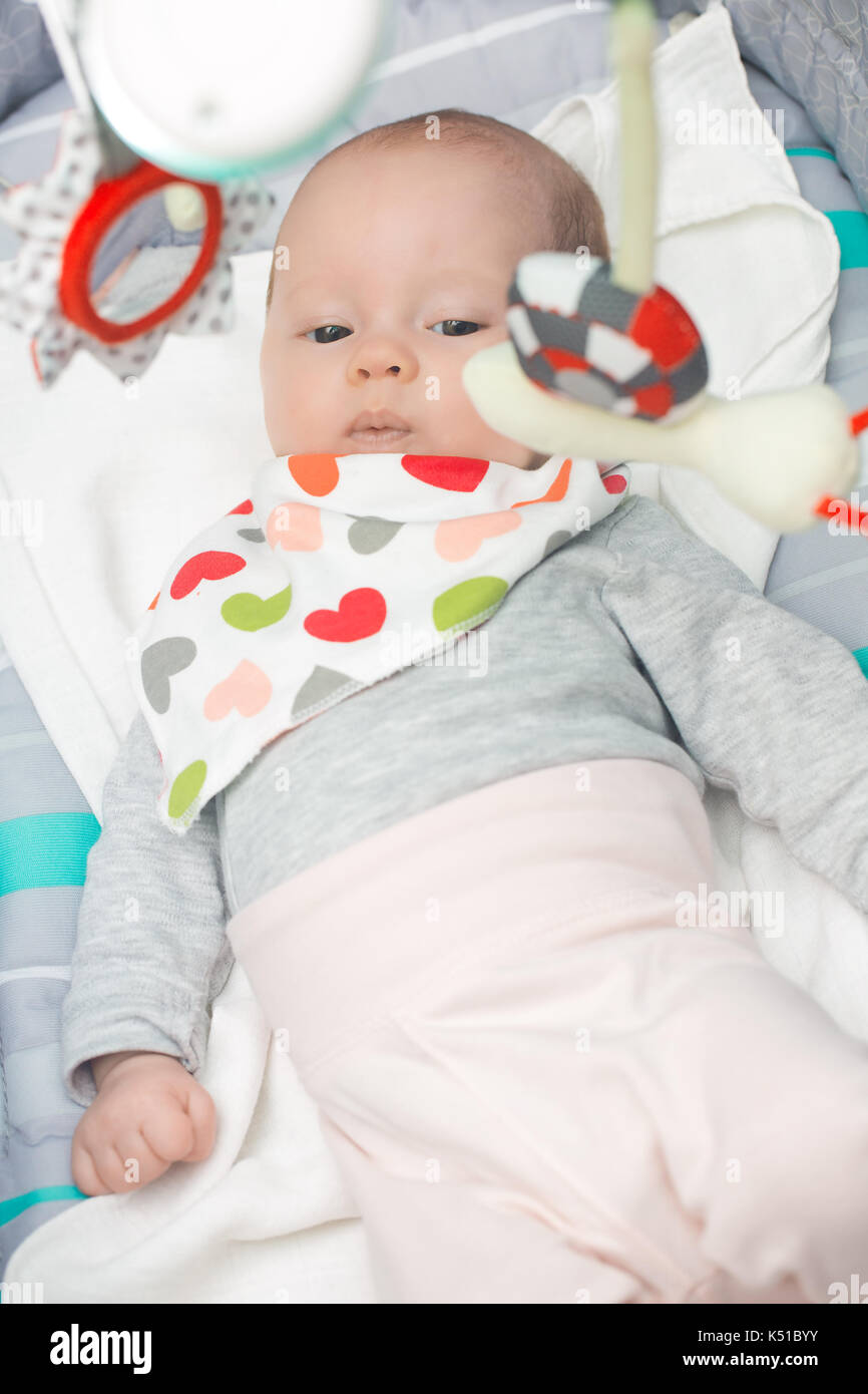 niña de 4 meses en asiento de bebé con juguetes mirando al lado