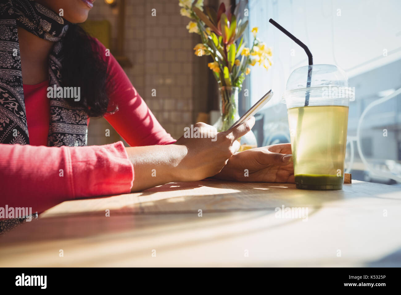 Sección intermedia de mujer con bebida con teléfono en el alféizar de la ventana en el café Foto de stock