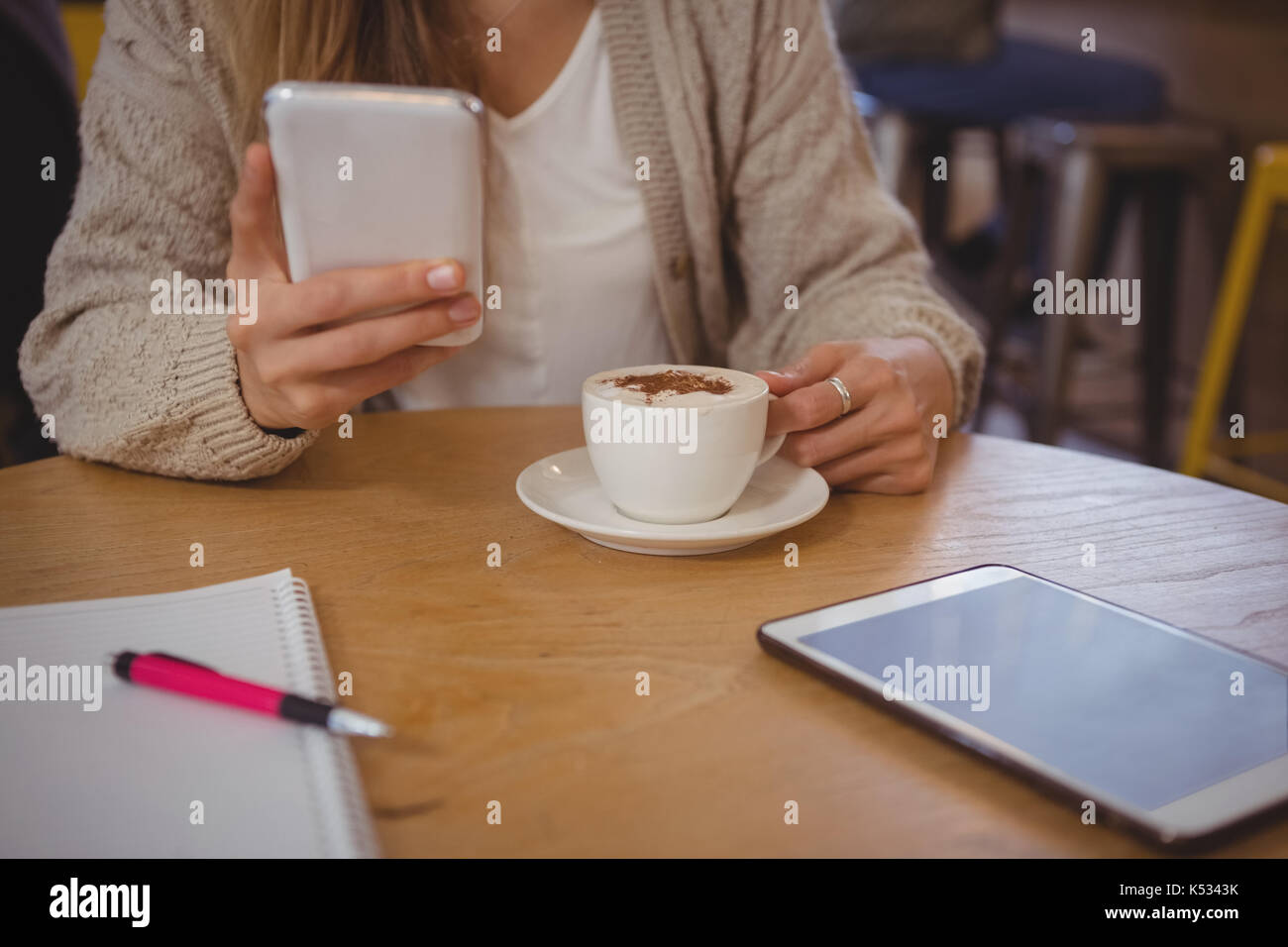 Sección intermedia de mujer con café utilizando el teléfono en la mesa del café Foto de stock