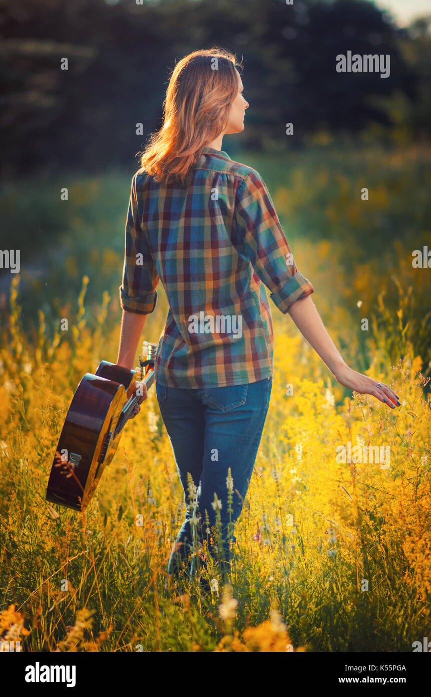 Joven con una guitarra acústica, paseos por el campo en otoño al aire libre  al atardecer. vista desde la parte de atrás Fotografía de stock - Alamy